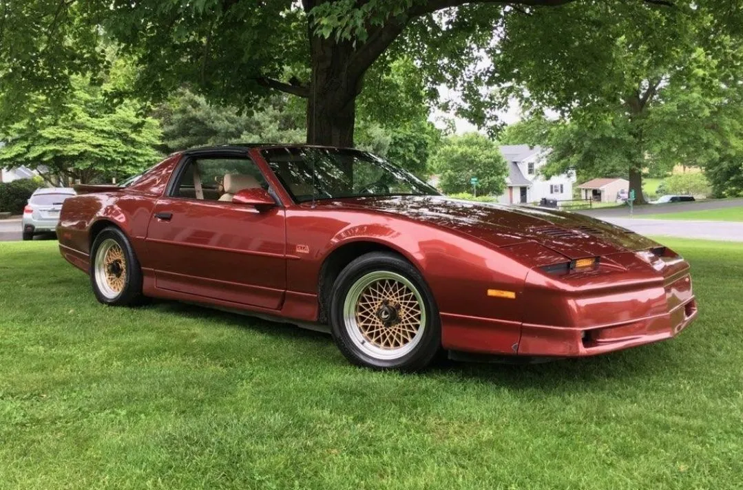 A red 1987 Pontiac Trans Am GTA parked on the grass