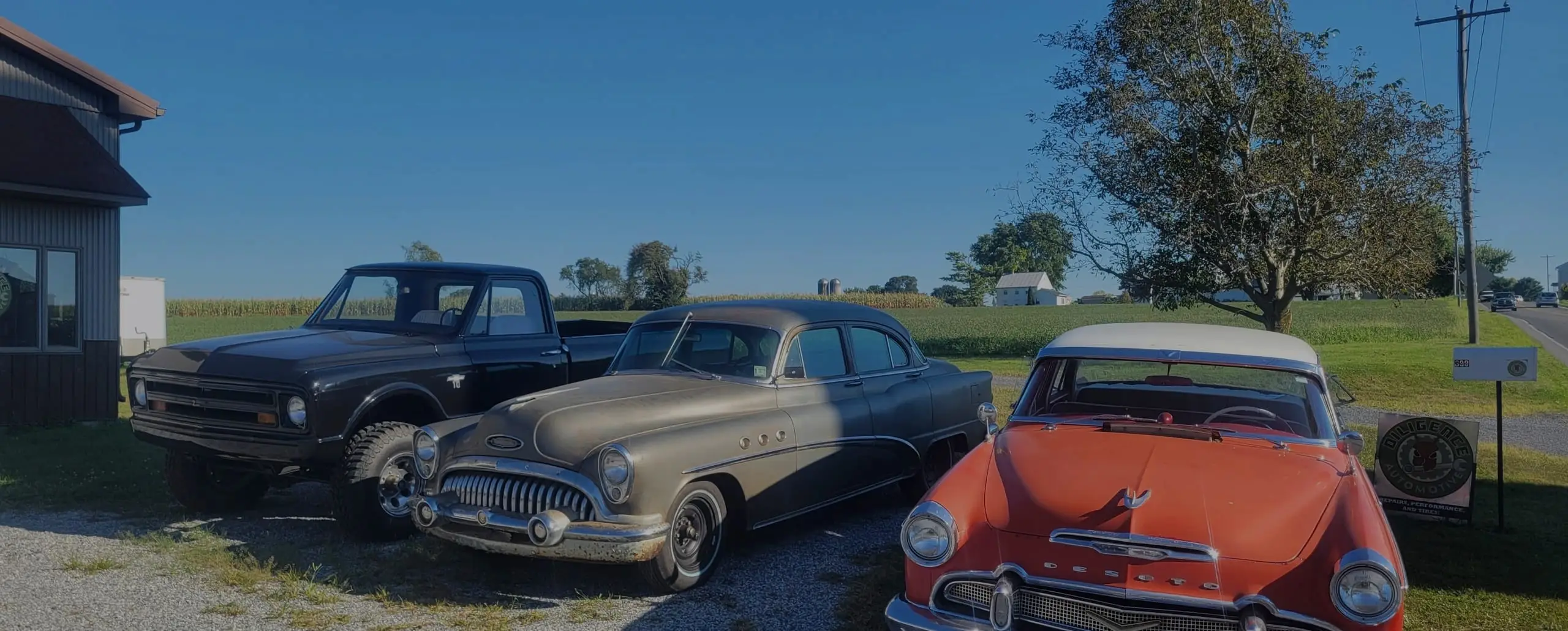 A classic Chevrolet pickup, Buick, and Dodge lined up outside the shop