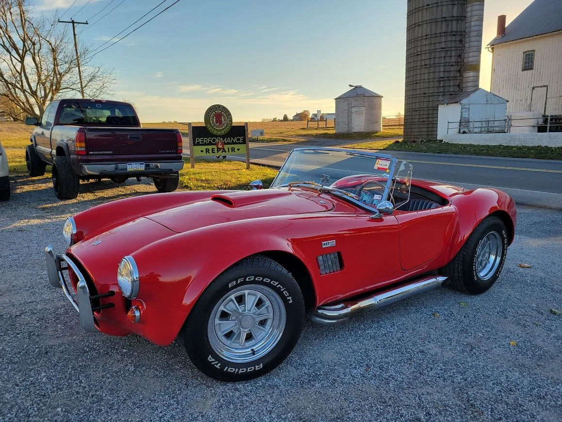 A red Cobra kit car parked outside the shop