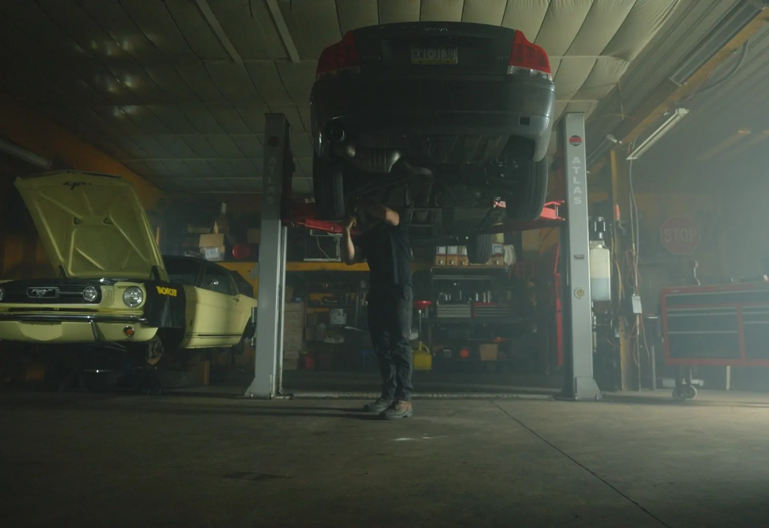 A technician working under a car on a lift inside the Diligence Automotive shop